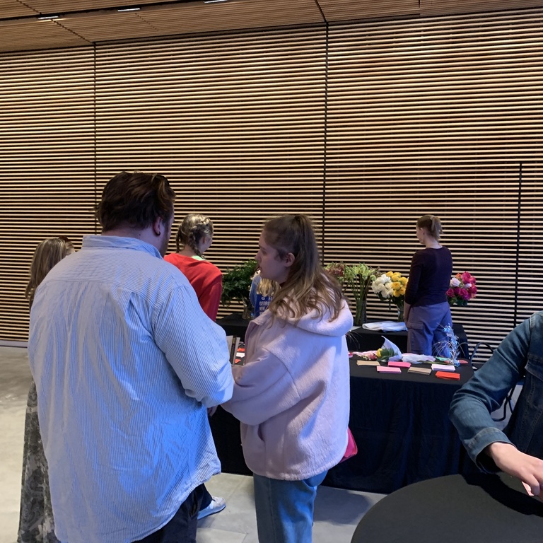 shown are students standing at cocktail tables. some students are also in line to make their own bouquets 