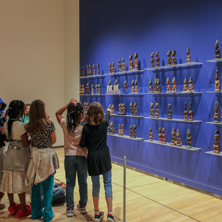 Group of children standing in a gallery in front of a blue walls with African art on display