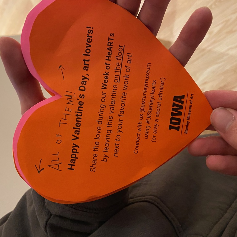 A hand holding a heart that says "all of them" written on it. 