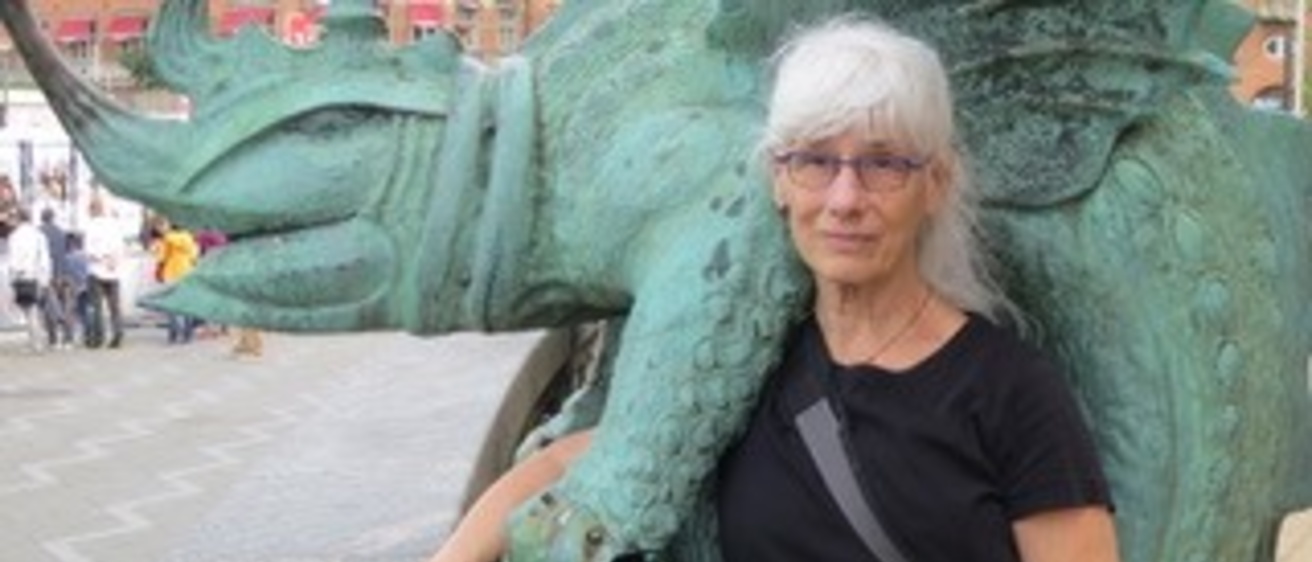 Woman with silver hair and glasses stands with a patinated bronze statue.