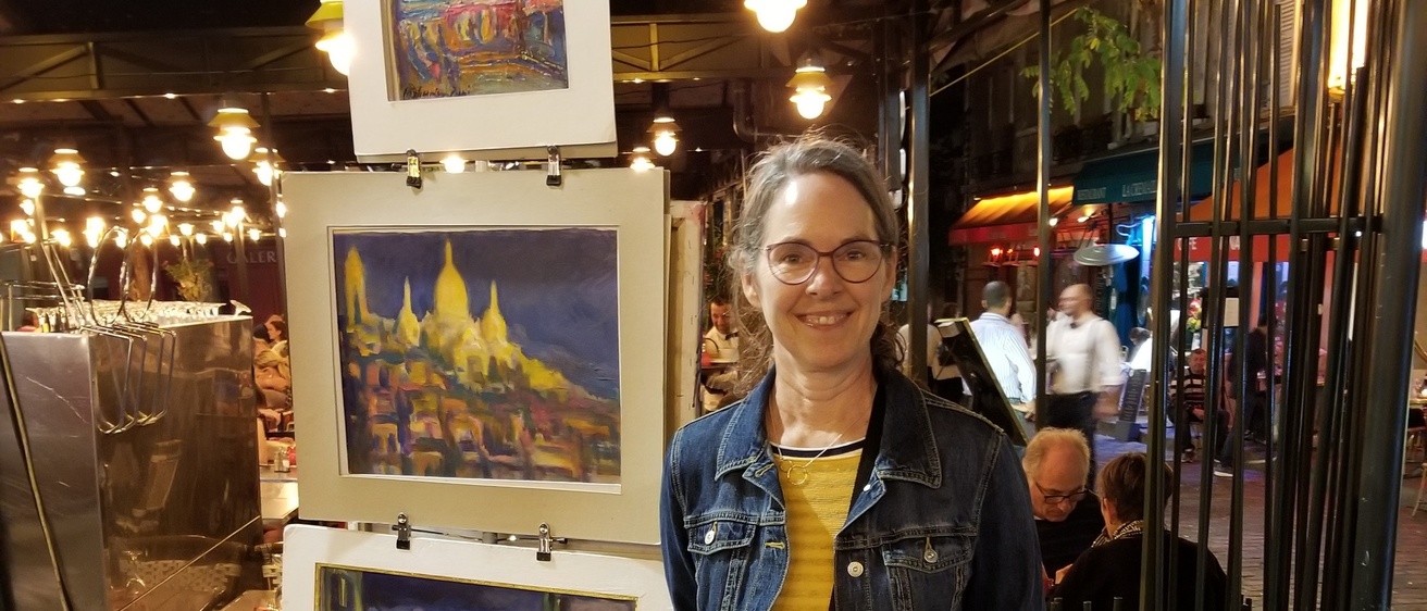 woman stands next to a rack of art prints in an outdoor market