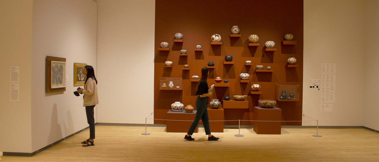 Student walks along a display of Southwestern ceramics, which are displayed against a medium burnt umber background