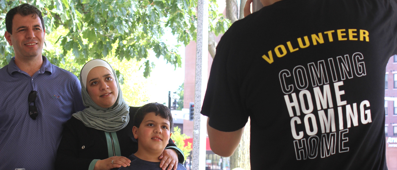 A man wearing a black t-shirt that reads "Volunteer" takes a photo of a family