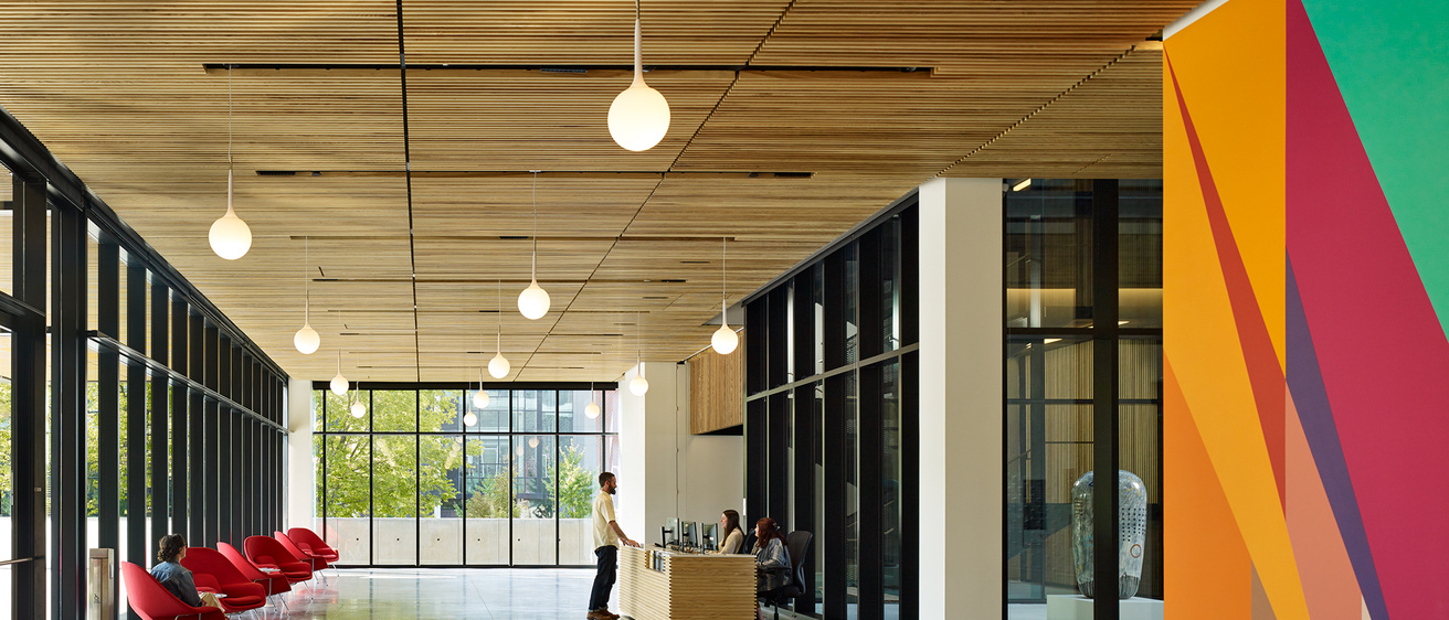 Large, airy lobby with full-height windows, red arm chairs, and a brightly painted wall 