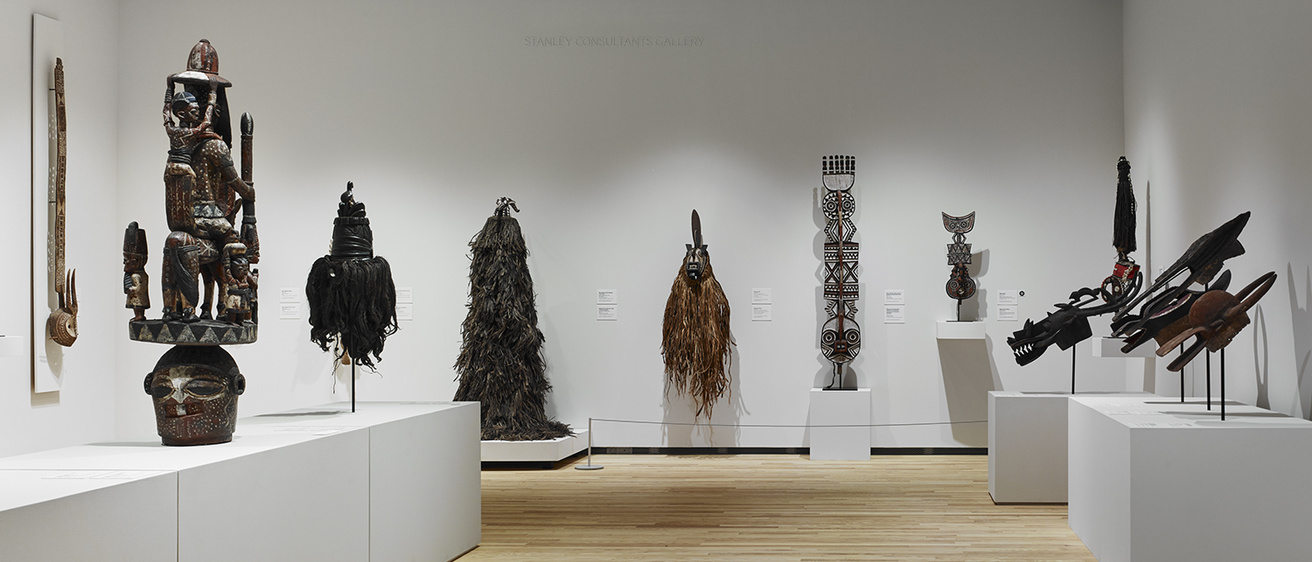 A gallery with white walls and light, wood floors displays African masks.