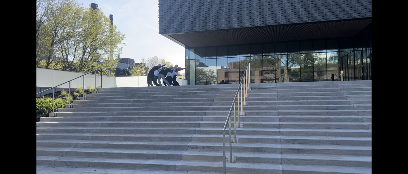 A still image from a video of a dance project choreographed by Katherine Shamdin. In it, 5 students dance on the front steps of the Stanley.