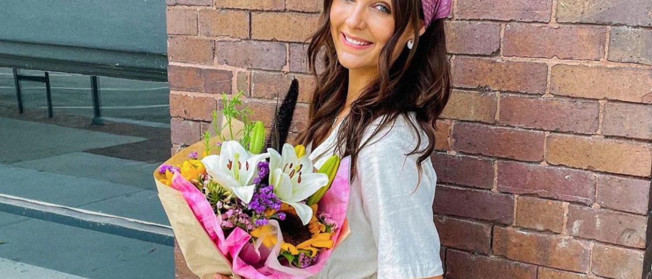 A photo of Aubrie, posing with a bouquet of flowers in front of a brick wall.