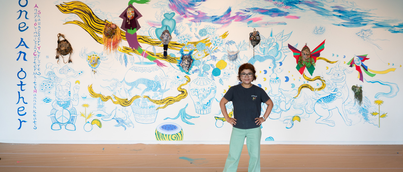 A person standing in front of a wide wall filled with drawings and painting