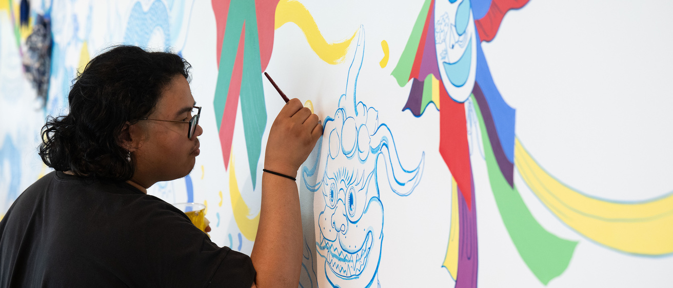 A photo of Stanley student employee, Shaun Mallonga, working on Jiha Moon's mural, 'One An Other,' in the Stanley Museum of Art lobby.