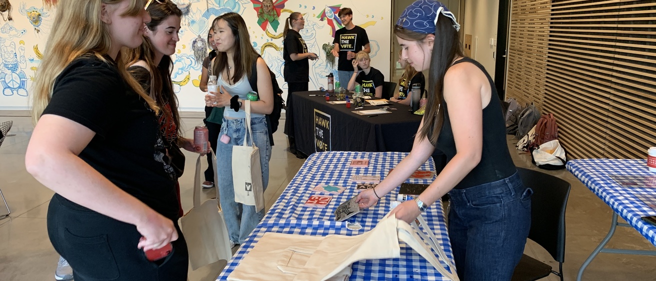Students wait and watch as Annelies block prints voting-inspired imagery onto tote bags, pencil cases, fabric patches, or other fabric items at the direction of the students.