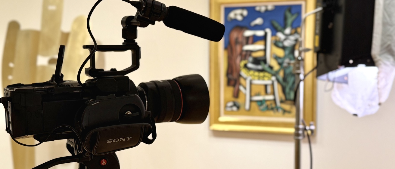 A camera with a mic attachment directed at a painting on a wall