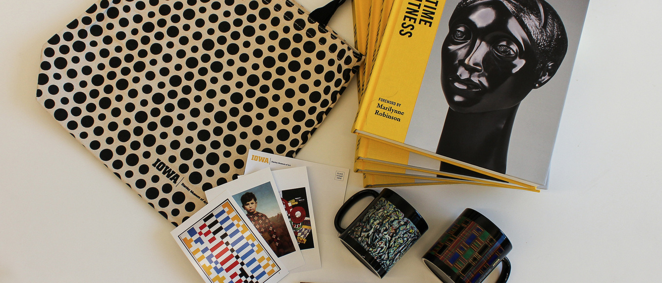 A tote bag, mugs, a book, postcards and pencils displayed on a surface