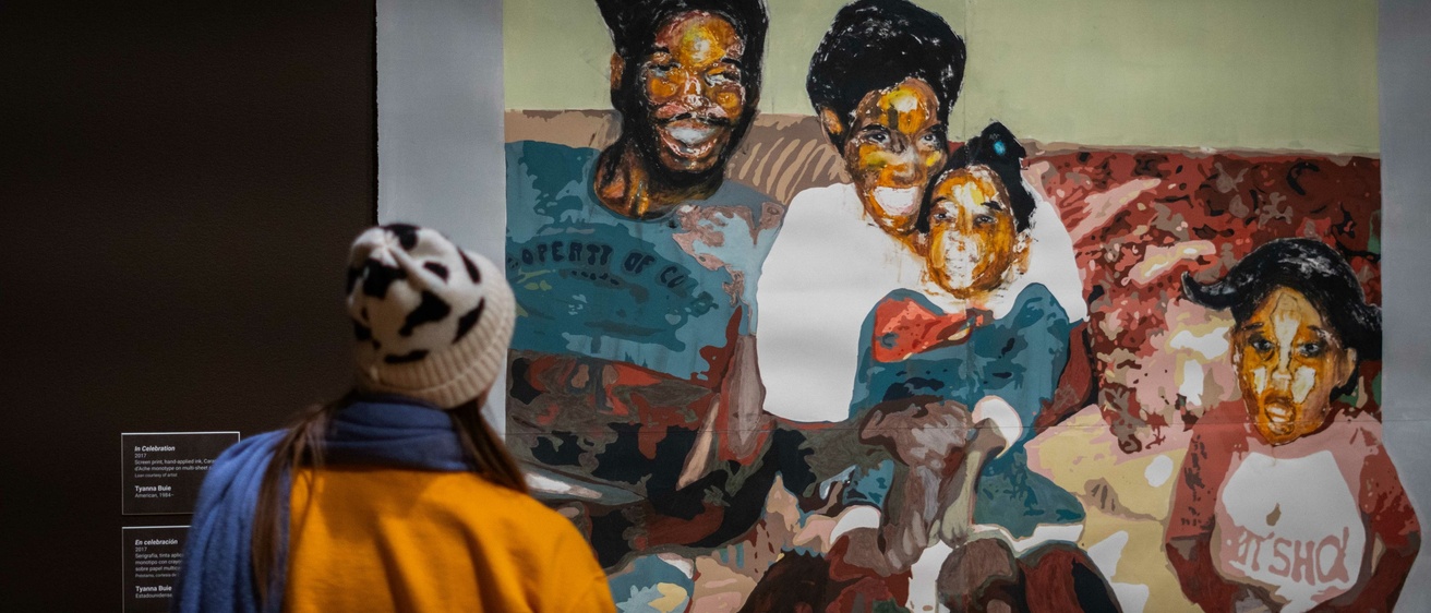 A person views a large colorful painting of a black family displayed in a museum