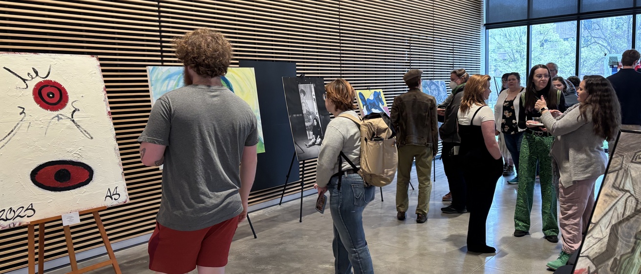 A group of people explore artworks on display at the 2025 Student Exhibit.