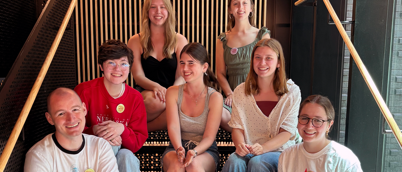 Seven graduating senior student employees sit on the stairs at the Stanley Museum of Art.