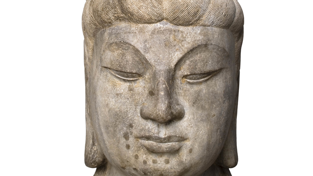 Carved head with tranquil face, eyes looking downward, and an elaborate headpiece