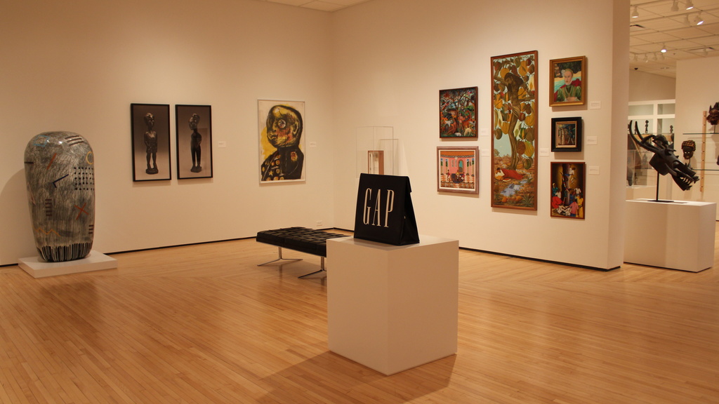 museum gallery with artworks on walls and sculptures and a bench in the middle of the space