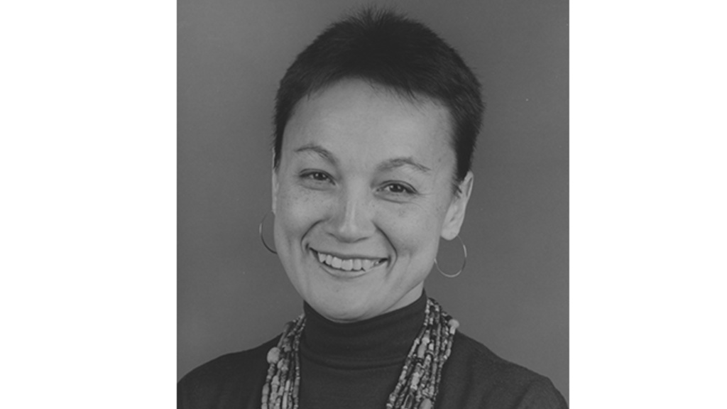 Black and white portrait of a smiling woman with very short dark hair wearing a dark top and many strands of African beads