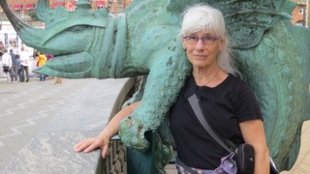 Woman with silver hair and glasses stands with a patinated bronze statue.