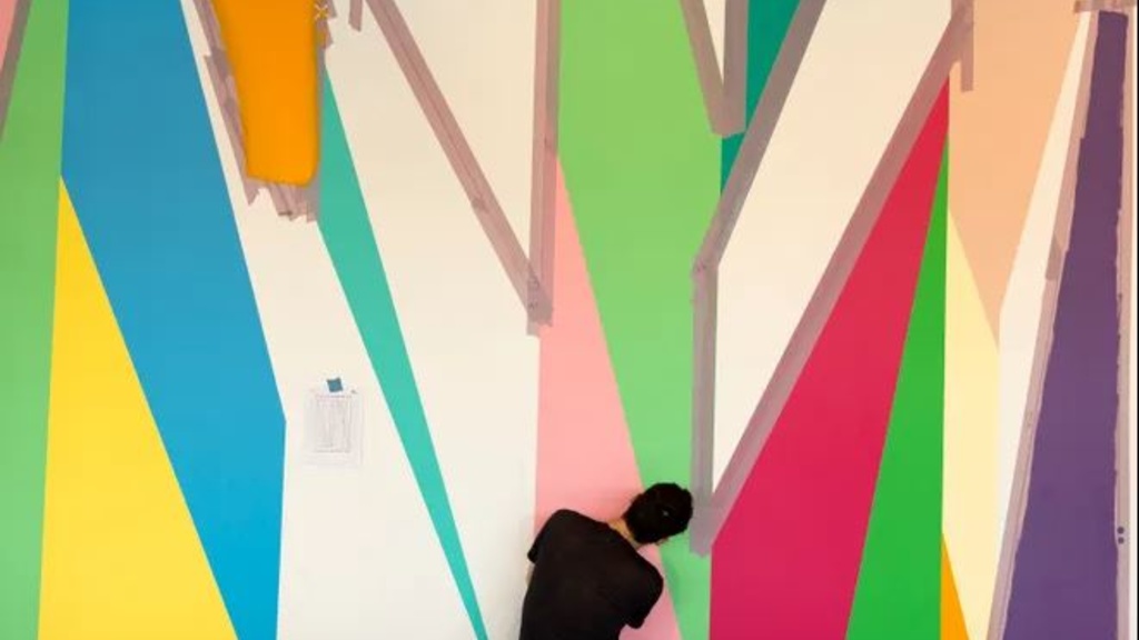 Person painting a wall with brightly colored, geometric shapes