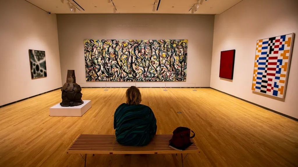 person seated on a bench looking at artwork in a museum gallery