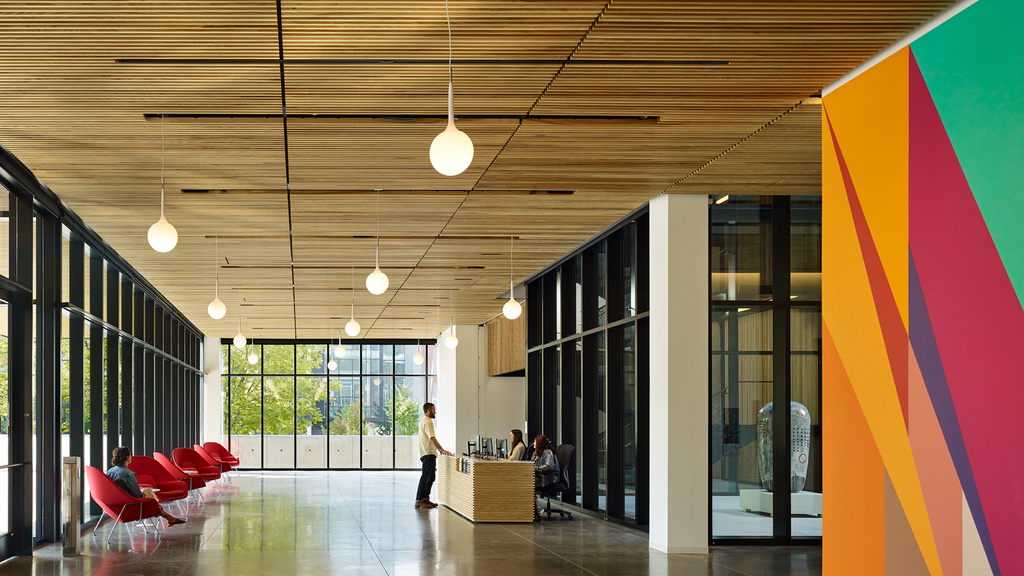 Large, airy lobby with full-height windows, red arm chairs, and a brightly painted wall 