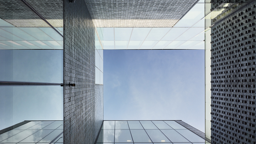 Looking up the lightwell past brick and glass walls toward a square of blue sky.