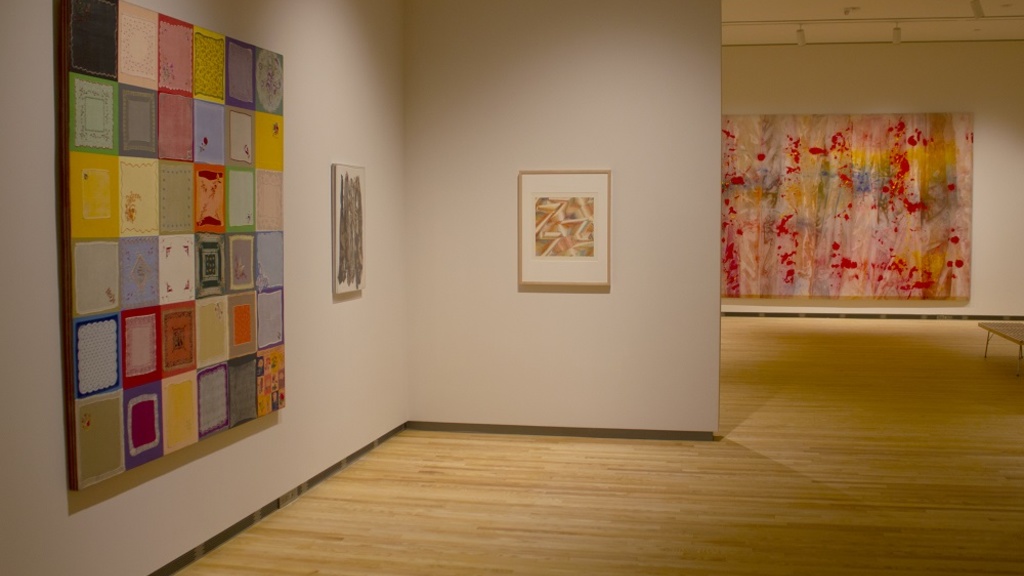 An installation shot of galleries 1 and 2 at the Stanley Museum of Art: you can see four works of art lit with warm light in the space.