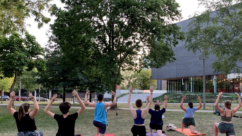Students doing yoga in Gibson Square Park. The photo is taken from behind, with the Stanley Museum of Art visible in the background.