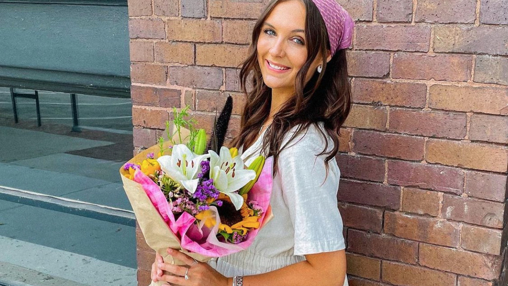 A photo of Aubrie, posing with a bouquet of flowers in front of a brick wall.