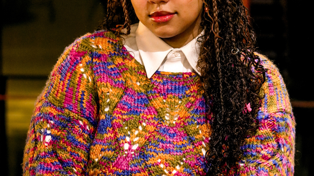 A photo of Lily Hester: they are posing in Art Building West, wearing a very colorful sweater.