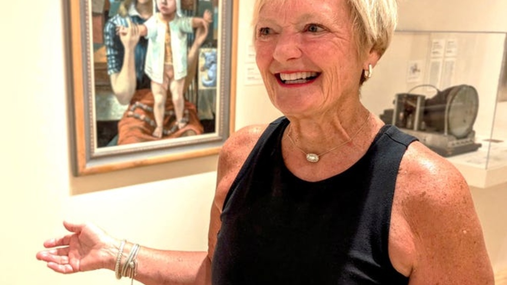 A photo of an older woman in a black tank top with short, blonde hair standing in front of Phillip Guston's "The Young Mother" at the Stanley Museum of Art.