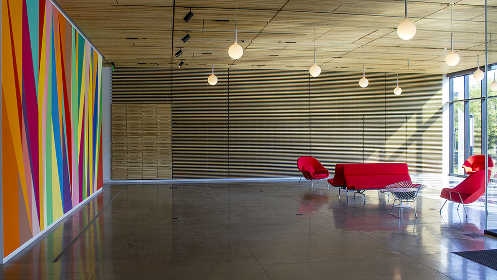 A long lobby with cement floors, red lounge chairs, dropped lighting fixtures, and natural light.