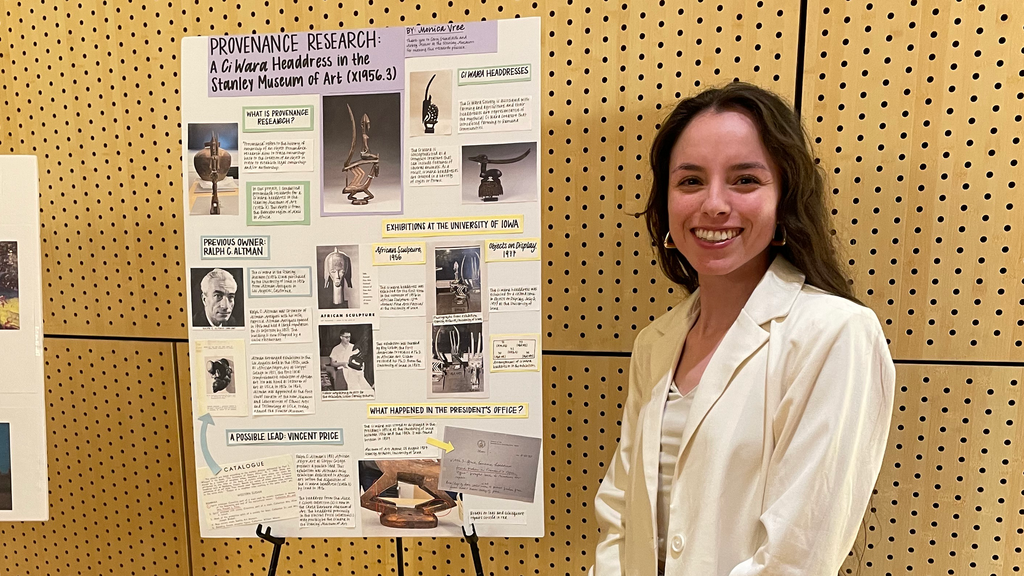 A photo of Monica standing beside a poster she made at the Iowa Arts Fest, detailing her work as part of Cory Gundlach's class.
