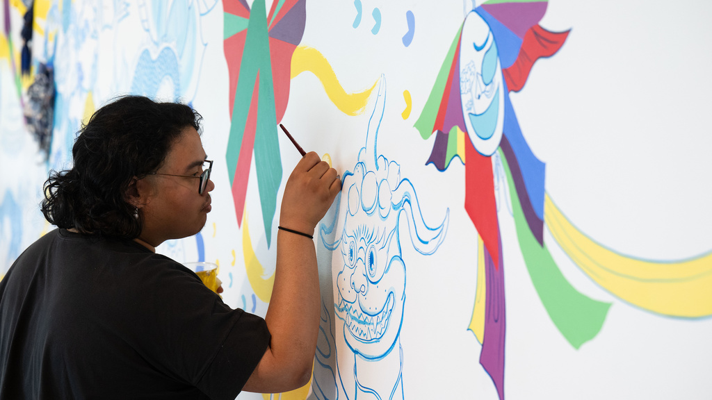 A photo of Stanley student employee, Shaun Mallonga, working on Jiha Moon's mural, 'One An Other,' in the Stanley Museum of Art lobby.