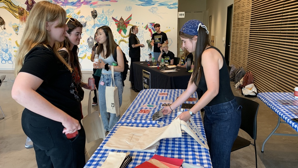 Students wait and watch as Annelies block prints voting-inspired imagery onto tote bags, pencil cases, fabric patches, or other fabric items at the direction of the students.