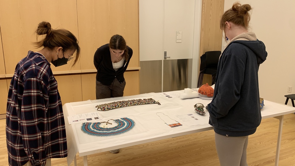 Three people stand over a desk with art objects placed on it 