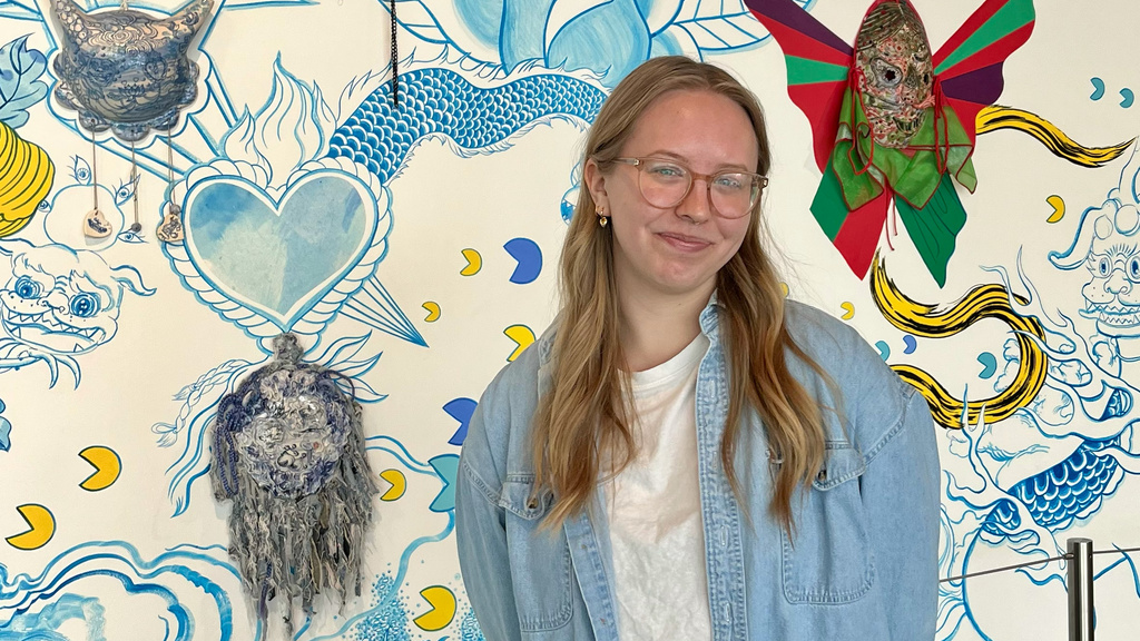 A photo of Josie, posing in front of the Jiha Moon mural in the Stanley lobby.