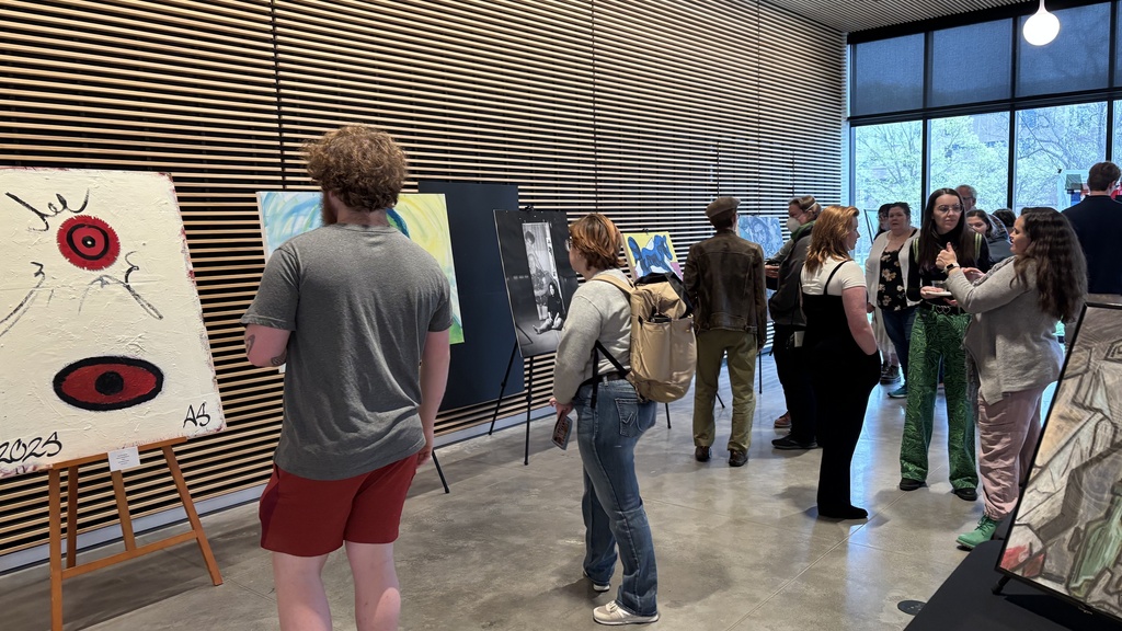 A group of people explore artworks on display at the 2025 Student Exhibit.
