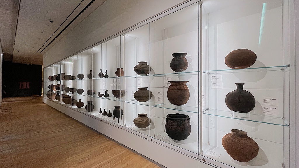 An extended wall with glass panels behind which are encased pottery of various shapes and sizes