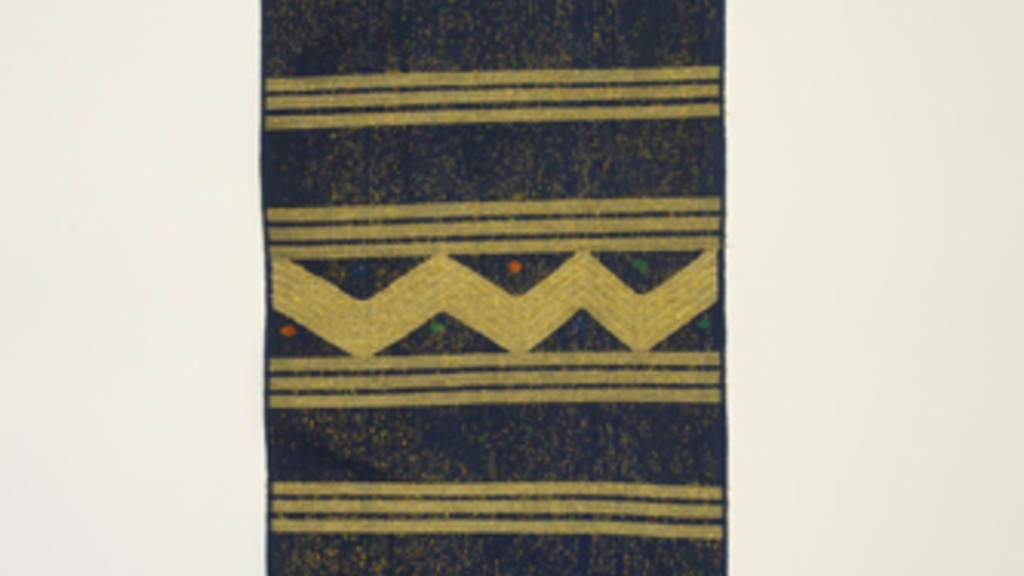 Long rectange of woven fabric with patterns of lines and zig-zag shapes in shiny gold and navy threads.