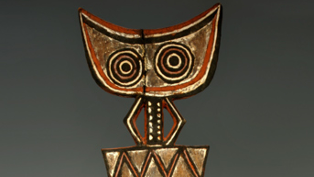 Wooden mask, divided into three main sections: an oval face with two very large round eyes, a diamond-shaped mouth, and a vertical hook which represents the bill of a hornbill, a rectangle decorated with two horizontal zig-zag lines, and a crescent moon shape with two more concentric circles.