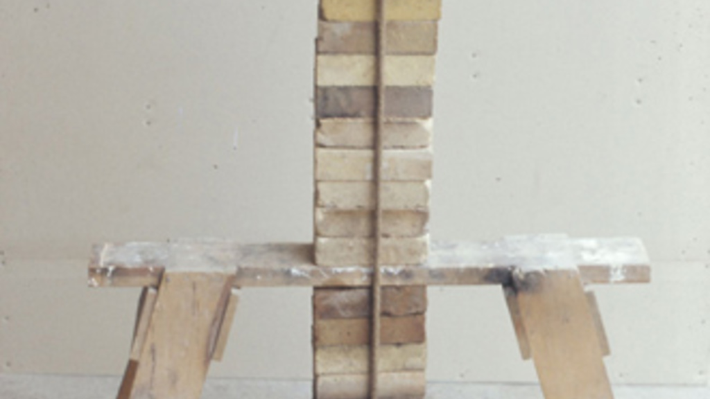 A wooden sawhorse with a column of bricks tied above and below.