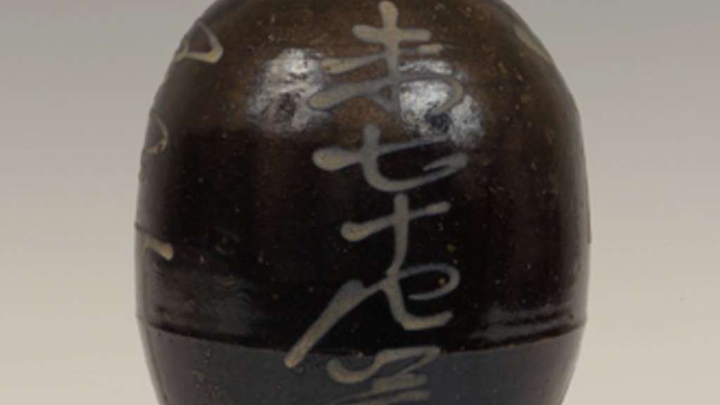 Oval-bodied vessel with short, narrow neck. The dark glaze is decorated with Japanese calligraphic characters.