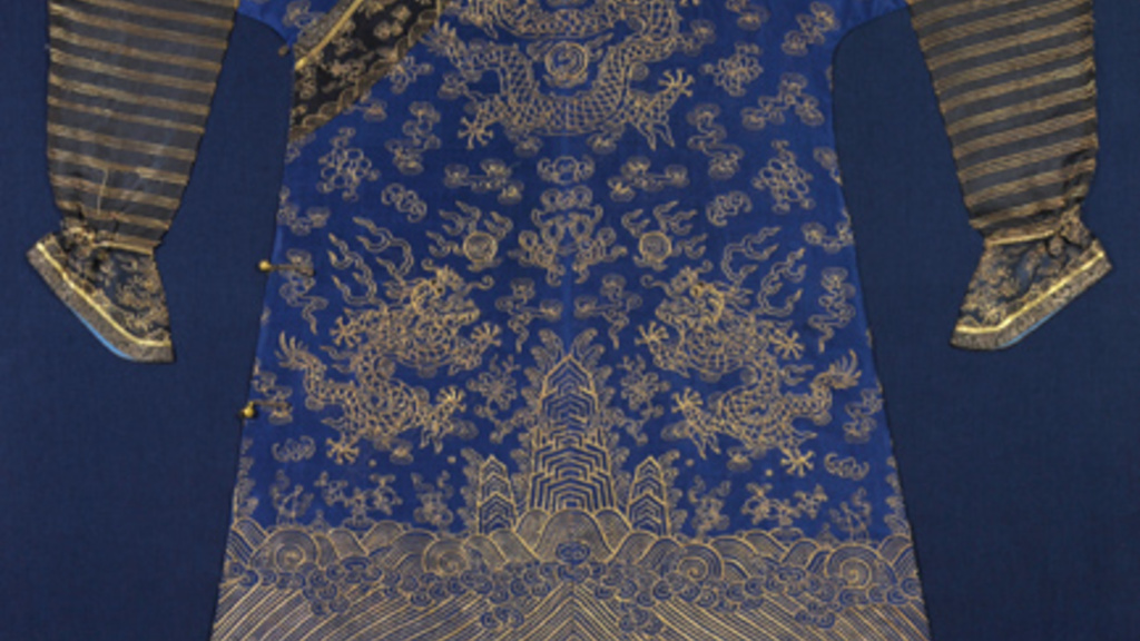 Silk robe in deep blue with metallic gold embroidery. It has bunched black sleeves with gold detailing. Eight gold metallic dragons fly across the blue fabric panel between swirling cloud, bat, and peony motifs, also in gold embroidery.