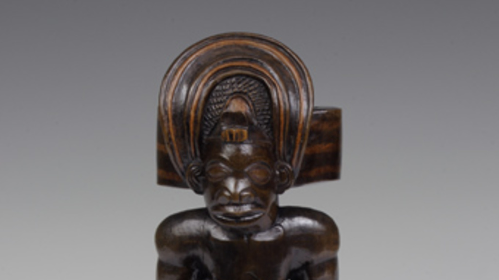 Wooden figure of a Chokwe chief wearing an elaborate crown and holding small figures of male and female ancestors.