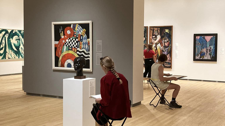 Students sit on stools sketching in front of artworks