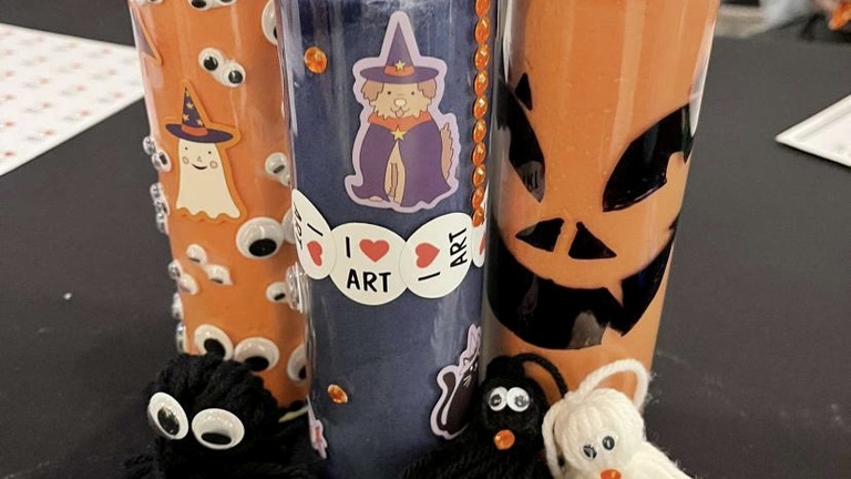 Another example of the event's crafts: Three votive candles (two orange and one purple) decorated with stickers, rhinestones, and markers, and then several pompom creatures with google eyes and other embellishments.