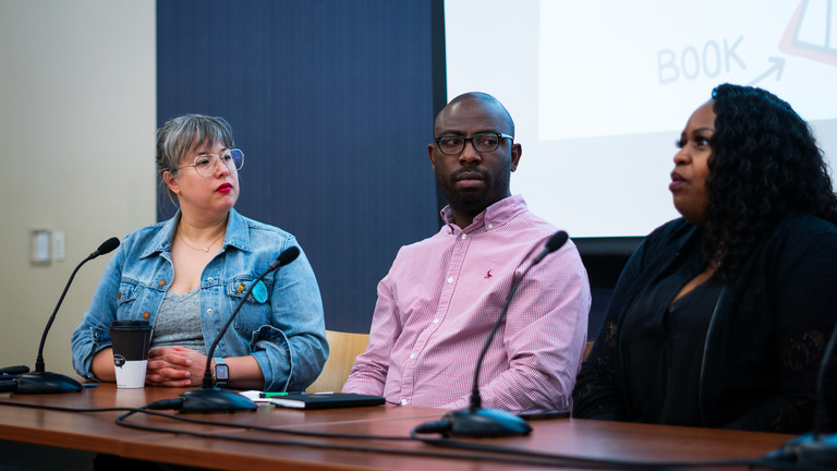 Three people sitting behind a table, conversing.